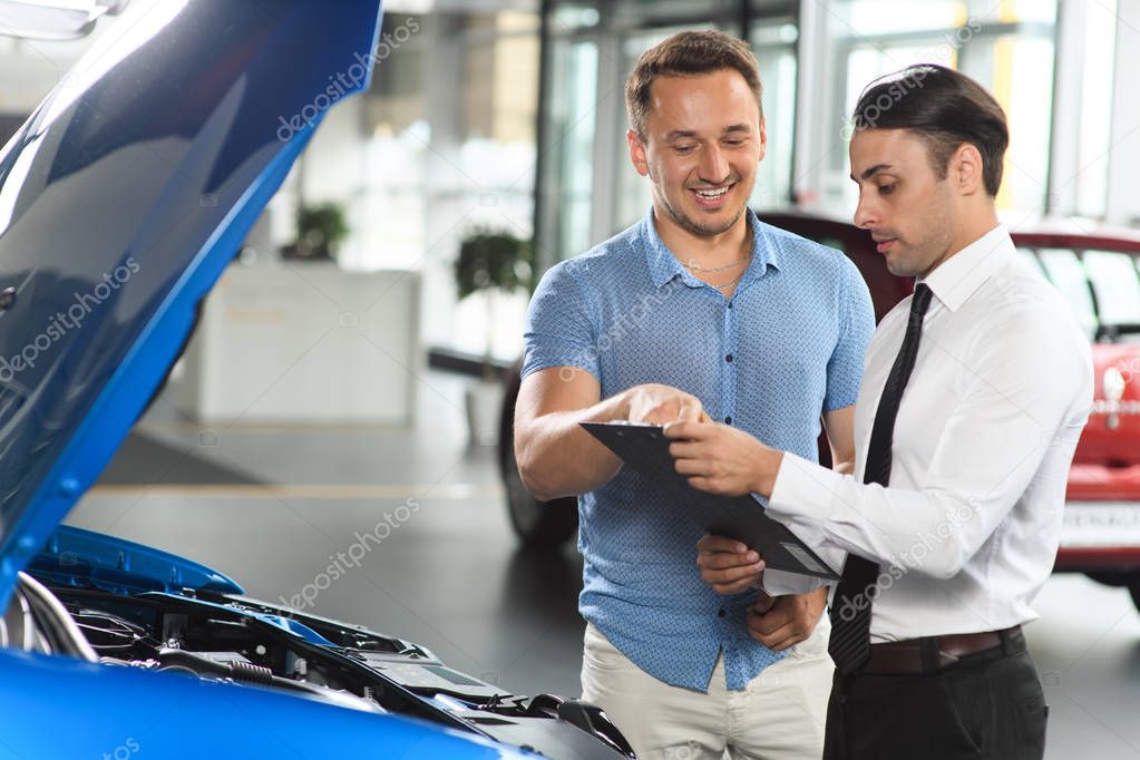 Salesman shows car engine for his client. Client  choosses possible engines on the tablet