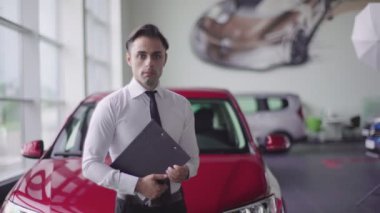 İstemciler için yol gösteren satıcısı. Gülümsüyor. Beyaz gömlek ve siyah kravat takıyor.