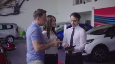 Çift yeni araba seçin. Müşteri ve satıcı el salla. Kız yeni satın alma çok mutlu olmak, gülümsüyor.