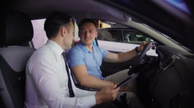 Satıcı için müşteri otomobil gösterileri. Onlar yeni arabanın içinde oturuyorlar. Araba mavi. 