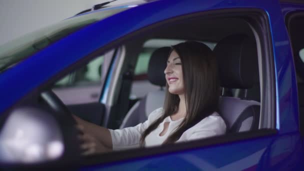女の子は 新しい車に座っています 車は青色です 彼女は努力してステアリング ホイールをどのように感じています — ストック動画