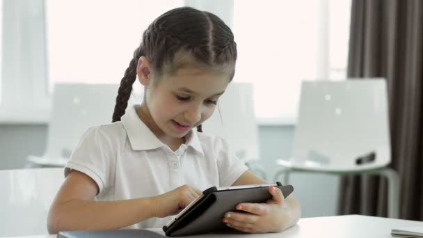 那个带辫子的小女孩正在看平板电脑 她穿着一件白衬衣 她有两个辫子 — 图库视频影像