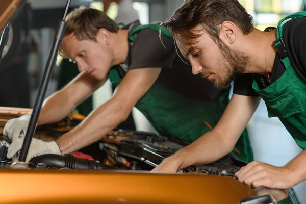 Dos Jóvenes Mecánicos Mono Verde Tratan Arreglar Motor Coche Naranja —  Fotos de Stock