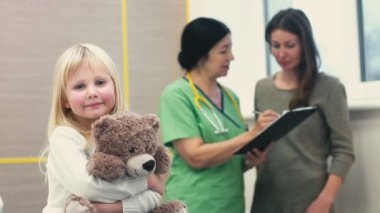 Doktor ziyaret. Sevimli küçük şirin kız çocuk doktoru için arka plan boşaltmak Hastanesi klinik tıp sağlık ebeveynlik üzerinde ona anne kameraya gülümseyen onun oyuncak ayı kucaklayan