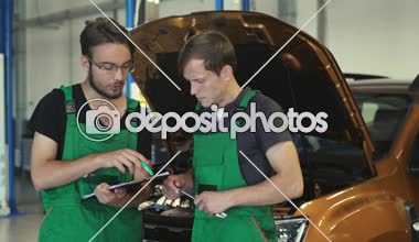 İki genç mekaniği-çocuklar, arabada durumunu tartışmak. Arka planda turuncu bir araba yeşil tulum giymiş.