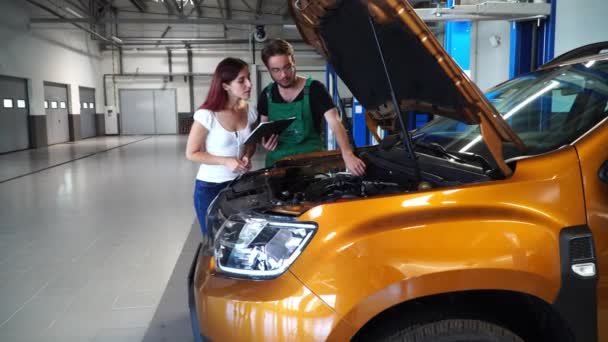 Mecánico Muestra Chica Que Necesita Ser Reparado Coche Naranja — Vídeo de stock