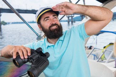 Sakallı genç bir adam onun ellerinde dürbün ile yönetiminde bir yatta yelken