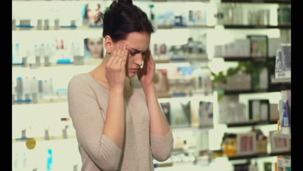 若い女の子が彼女の頭を保持している薬局を歩く 彼女は頭痛を持っています — ストック動画