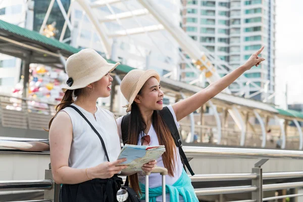 Young Asian tourist woman pointing at the building while her friend looking and holding a map