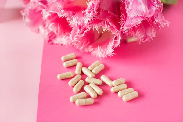 vitamins capsules on pink background with tulips