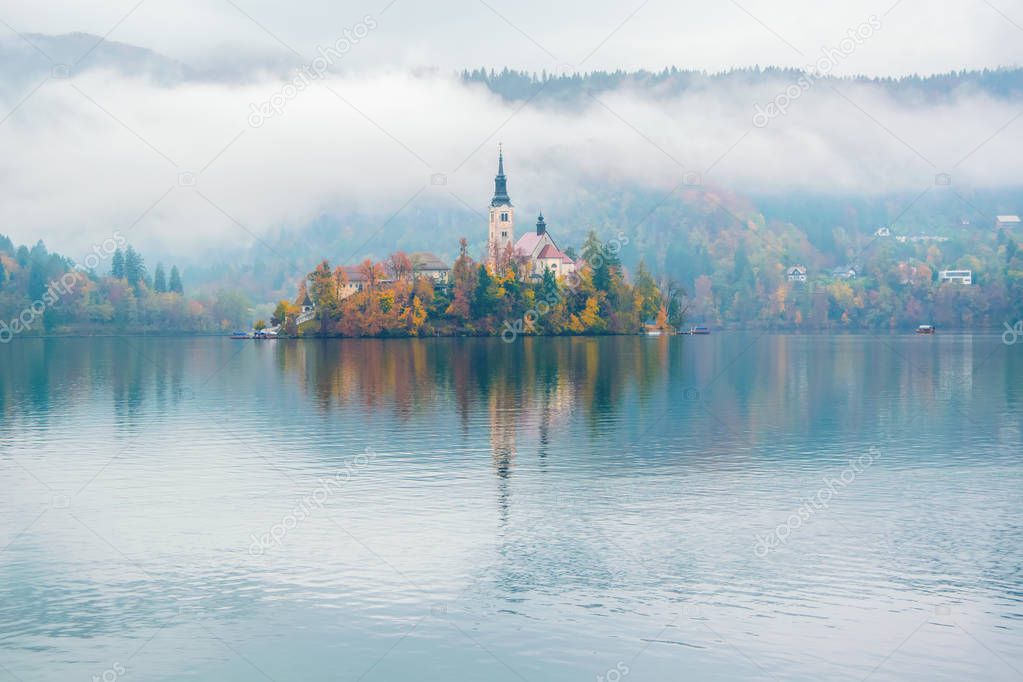 Amazing view of Lake Bled at foggy autumn morning with pilgrimage church of the Assumption of Mary on Bled island reflected in water, Slovenia