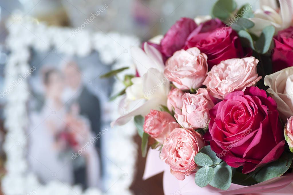Bridal bouquet of red, pink and white roses near photo of newlyweds in frame