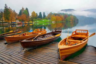 Lake Bled quay ile renkli ağaçlar üzerinde demirleyen tekneleri ve sis om arka plan Slovenya kaplı dağları ile sonbahar sahne