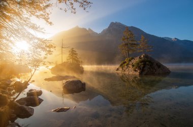 Sonbahar sabahı şaşırtıcı güneş doğarken Hintersee göl kenarında. Çam ağaçları taş suda yansıyan. Sis su üzerine yayılır. Sihirli tablomsu sahne Berchtesgaden Alpleri, Almanya