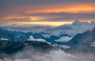 Renkli gökyüzü altında bulutlar tarafından kaplı dağları ile Dolomities içinde güzel günbatımı manzaralı görünüm