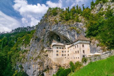 Slovenya 'nın Postojna kenti yakınlarındaki mağara ağzındaki Predjama kalesinin güneşli yaz günündeki manzarası