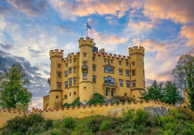Gün batımında Bavyera, Almanya 'da yanan gökyüzünün altında Hohenschwangau Kalesi' nin muhteşem manzarası. Hohenschwangau Şatosu ünlü Neuschwanstein Peri Masalı Kalesi yakınlarında popüler bir seyahat merkezidir.