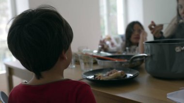 Küçük çocuk yemek masasında ailesiyle yemek yerken insanlar samimi ve özgün bir şekilde toplandı. Koltuğundan aile üyelerini izleyen çocuk