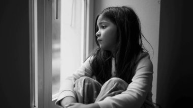 Depresyondaki küçük kız pencereden bakıyor, dramatik siyah-beyaz, çocukluk zihinsel hastalığında kayıp ve üzgün.