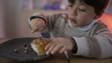 Çocuk bıçakla bir parça ekmek kesiyor. 5 yaşındaki çocuk tabakta karbonhidrat yemeği dilimliyor.
