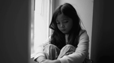 Depresyondaki küçük kız pencereden bakıyor, dramatik siyah-beyaz, çocukluk zihinsel hastalığında kayıp ve üzgün.
