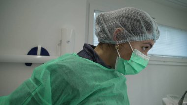 Kadın Dişçi Doktor klinik antiseptik üniforma giymeye hazırlanıyor. Önlük, maske ve başlık takan kadın.
