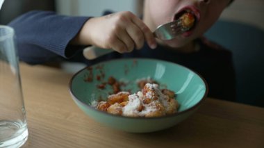 Yemek saatinde tabakta gnocchi yiyen küçük bir çocuk. Düşünceli 5 yaşındaki çocuğun yakından çekilmiş yüzü çatalla yemek yiyor.