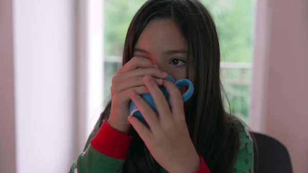 Little girl drinking warm drink during cold day indoors. Child sipping hot choco to stay warm during winter season