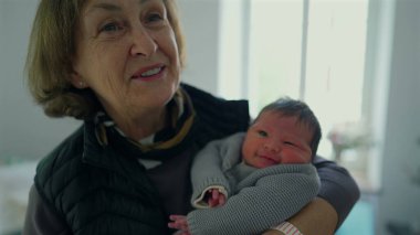Büyükanne yeni doğmuş bir bebeği kucağında tutuyor, nazik bir gülümsemeyle, sevgi ve bağlılık anını yakalıyor, nesiller boyunca aile bağlarını ön plana çıkarıyor..