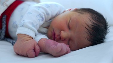 Yeni doğan bebek yumuşak bir yatakta huzur içinde uyuyor. Huzurlu bir ortamda çocukluğun huzur ve narin güzelliğini gösteriyor..