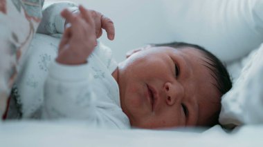 Yeni doğmuş bir bebek yatakta yatarken yakından ağlıyor. Bebeğin yüzü sıkıntılı, gözleri kapalı ve ağzı açık, rahatsız edici..
