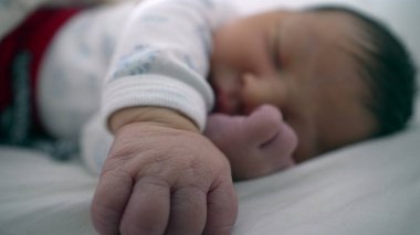 Yeni doğan bebek bir eli açık, diğer eli yüzü yakın bir şekilde bir yatakta huzur içinde uyuyor. Çocuğun sakin ifadesi ve rahat duruşu bir anlık sakinlik ve güvenlik-SD 480p 'sini vurguluyor