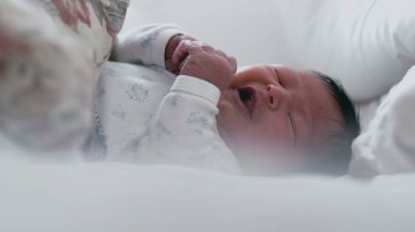 Uykulu bir ifadeyle ve yarı açık gözlerle yatakta yatan yeni doğmuş bir bebek. Bebek huzur içinde dinleniyor. Yüzlerinde yumuşak bir odaklanma, sakin ve huzurlu bir an.