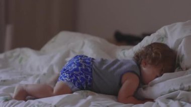 Bebek yataktan kayıyor ve yanında duruyor, evde neşeli bir an, merak ve enerjiyle çevreyi keşfediyor.