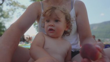 Yaz pikniği sırasında kucağında şeftali tutarak annesinin kucağında oturan küçük çocuk, tuhaf bir ifadeyle başını kaldırdı, sıcak ve hassas, sevgi ve bağlılık dolu bir aile anı..