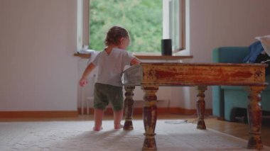 Oturma odasındaki küçük ahşap masanın etrafında daireler çizerek yürüyen çocuk, çevreyi keşfediyor, erken çocukluk merakı, hareket, öğrenme, bağımsızlık, aile hayatı