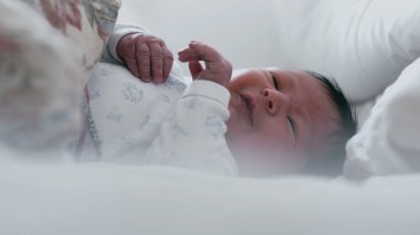 Uykulu bir ifadeyle ve yarı açık gözlerle yatakta yatan yeni doğmuş bir bebek. Bebek huzur içinde dinleniyor. Yüzlerinde yumuşak bir odaklanma, sakin ve huzurlu bir an..