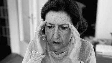 Şiddetli baş ağrısı olan yaşlı bir kadın, elleri şakaklara baskı yapıyor, derin konsantrasyon ve zihinsel gerginlik. Yaşlanan cilt ve yüz hatları, stres yoğunluğu, duygusal acı..