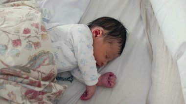 Yeni doğmuş bebek, yumuşak bir battaniyeye sarılı bir yatakta huzur içinde uyuyor. Bebek rahat, huzurlu bir konumda, sakin ve huzurlu bir anda..
