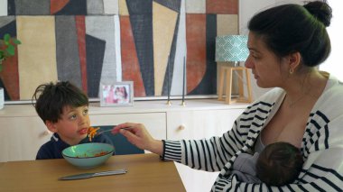 Kadın, bebeğini rahat bir evde emzirirken oğluna spagetti yediriyor ve aynı anda birden fazla çocuğa bakan bir annenin yoğun hayatını anlatıyor.