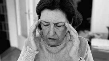 Şiddetli baş ağrısı olan yaşlı bir kadın, elleri şakaklara baskı yapıyor, derin konsantrasyon ve zihinsel gerginlik. Yaşlanan cilt ve yüz hatları, stres yoğunluğu, duygusal acı..