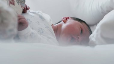 Uykulu bir ifadeyle ve yarı açık gözlerle yatakta yatan yeni doğmuş bir bebek. Bebek huzur içinde dinleniyor. Yüzlerinde yumuşak bir odaklanma, sakin ve huzurlu bir an..