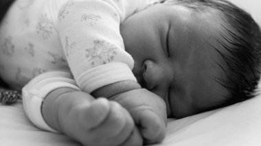 Uyuyan bir bebeğin siyah-beyaz yakın çekimi, erken çocukluğun ve huzurlu dinlenmenin hassas ve zamansız doğasını vurguluyor..