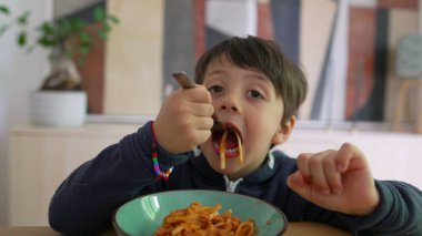 Yoğun odaklı bir çatal üzerinde spagetti çeviren küçük çocuk, sıcak bir ev ortamında yemek saatinde konsantrasyon ve kararlılık gösteriyor.