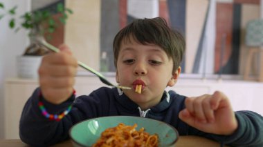 Yoğun odaklı bir çatal üzerinde spagetti çeviren küçük çocuk, sıcak bir ev ortamında yemek saatinde konsantrasyon ve kararlılık gösteriyor.
