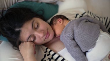 Anne yeni doğmuş bebeğini göğsünde tutarken huzur içinde dinleniyor. Sıcak bir ev ortamında kestirirken hassas bir anı yakalıyor. Yürek ısıtan bir sahne yaratıyor..