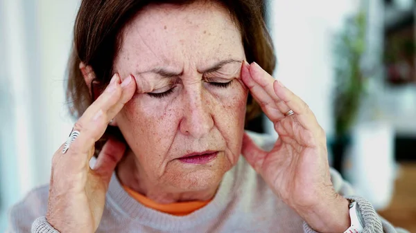 Olgun bir kadın şiddetli baş ağrısına katlanıyor, gözleri kapalı, elleri şakaklarda. İfade ve yüz hatları şiddetli acı, stres, zihinsel yorgunluk yükü, fiziksel veya duygusal gerginlik taşır..