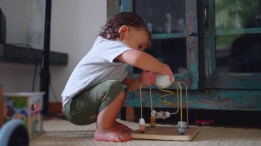 Küçük çocuk elinde çay fincanı, erken çocukluk merakı, öğrenme, gelişme, keşif, aile hayatı tutarken tahta eğitim oyuncağıyla oynuyor.