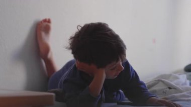 Genç bir çocuk yatakta uzanmış, kafa üstü uzanmış, akıllı telefon ekranına odaklanmış, sessiz ve huzurlu bir çocukluk anıydı.