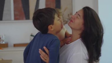 Bir annenin kıvırcık saçlı bir çocuğu kucağına alıp, kendinden büyük bir çocukla konuşması, duygusal stres ve günlük ebeveynlik sorunları gösteren sahneler.